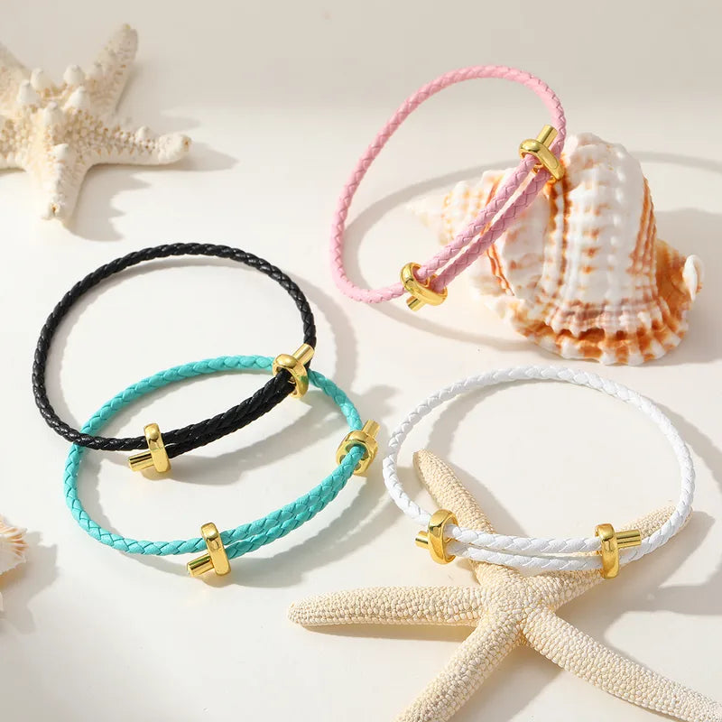 Vier Lederarmbänder in Schwarz, Rosa, Türkis und Weiß mit goldfarbenen Details, dekoriert mit Muscheln.