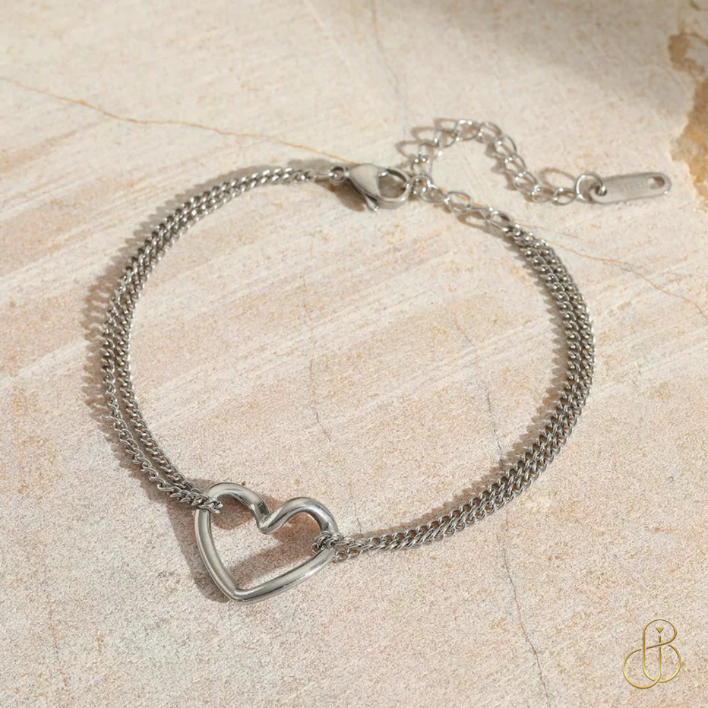 Herz-Armband Ella – 18K vergoldet, Edelstahl 304 & Kupfer – silberne Variante auf Steinoberfläche dekorativ präsentiert.