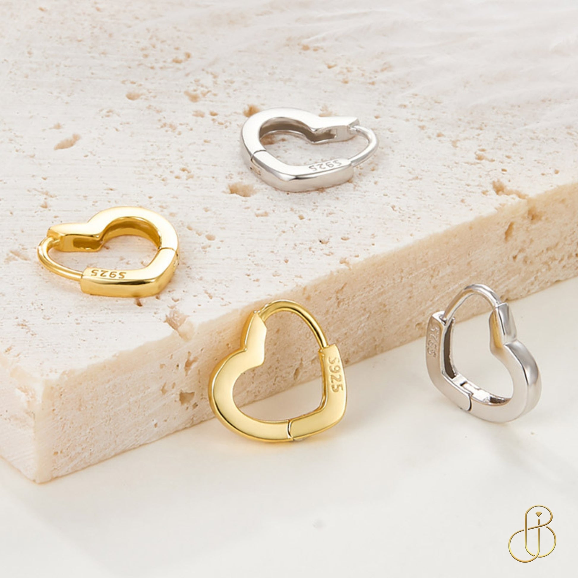 Vier Creolen in Herzform aus 925 Sterling Silber, teils vergoldet, auf Steinuntergrund dekorativ arrangiert.