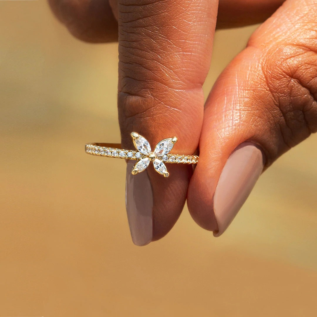 Schmetterlingsring aus 925er Silber mit funkelnden Zirkoniasteinen, in goldener Ausführung zwischen zwei Fingern gehalten.